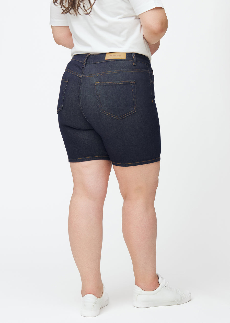 Tief dunkelblaue Denim-Shorts für Damen in der Farbe Midnights von hinten auf einem Plus-Size-Model gesehen, sodass die Länge bis zur Mitte des Oberschenkels sichtbar ist.