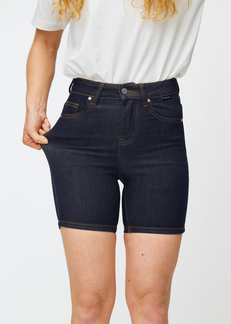 Model dehnt tief dunkelblaue Denim-Shorts für Damen in der Farbe Midnights am Oberschenkel, um den Stretch des Materials zu zeigen.