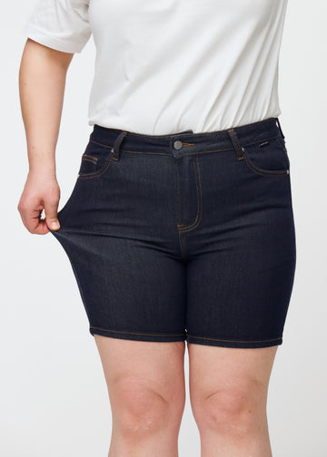 Plus-Size-Model dehnt tief dunkelblaue Denim-Shorts für Damen in der Farbe Midnights am Oberschenkel, um den Stretch zu zeigen.