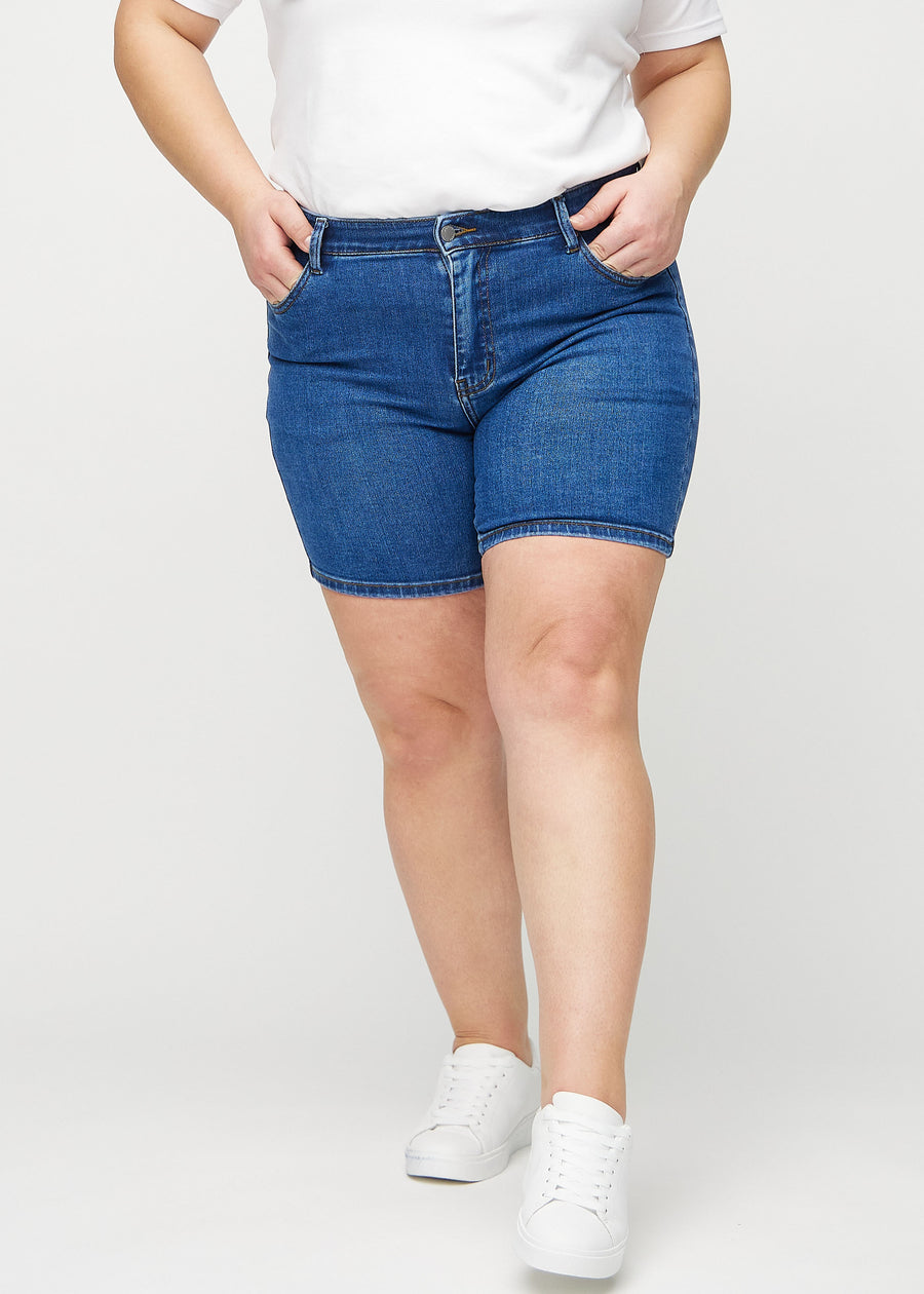 Dunkle Denim-skinny Short Shorts, Modellname Oceans, die eng anliegen und bei einem Plus-Size-Model bis zur Mitte des Oberschenkels reichen, von vorne gesehen.