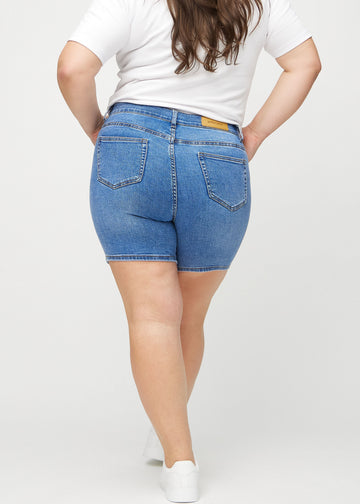 Denim skinny Short Shorts von hinten an einem Plus-Size-Model gesehen, sodass man das gesamte Produkt sehen kann.