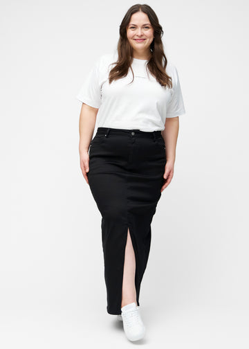 Fuldt billede af plus-size model i lang, sort jeansnederdel i farven Ravens med regulær pasform og slids foran.