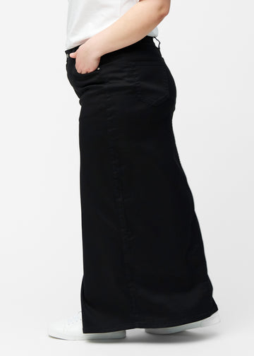 Lang, sort jeansnederdel i farven Ravens med regulær pasform set fra siden på plus-size model, med synligt slids foran.