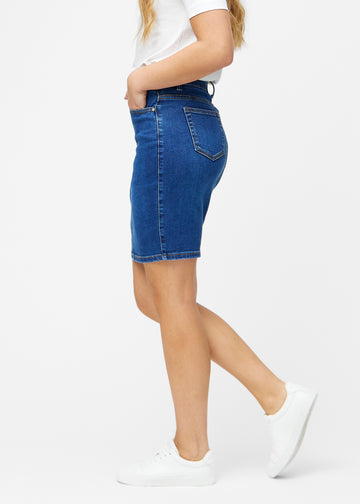 Mørkeblå, tætsiddende og knælang denimnederdel set fra siden på model.