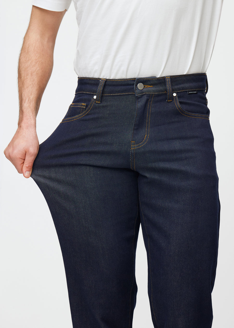 Das Model dehnt die tief dunkelblaue Denim jeans für Herren in der Farbe Midnights am Oberschenkel, um die Stretchqualität des Materials zu zeigen.