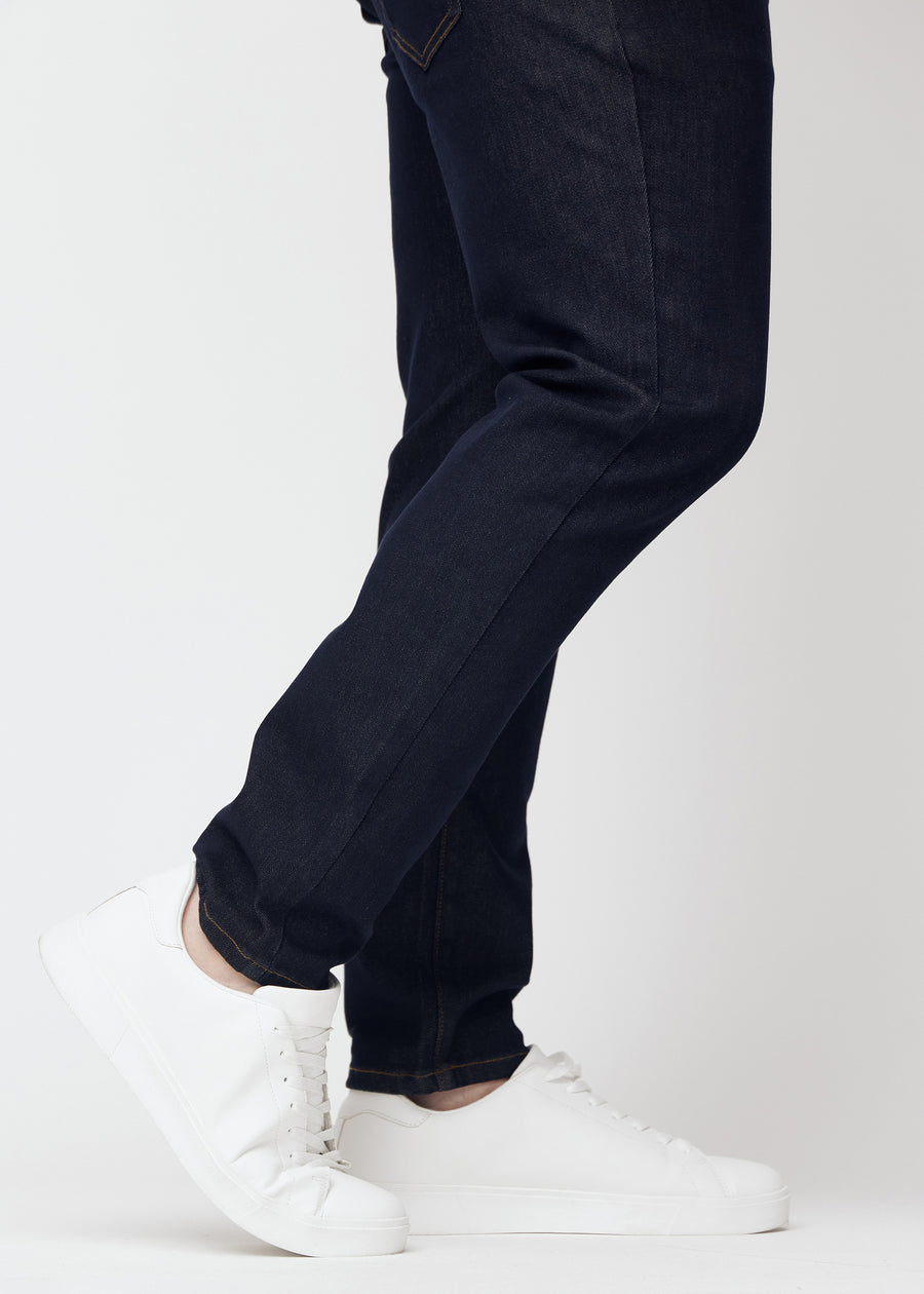 Tief dunkelblaue Denim jeans für Herren in der Farbe Midnights mit slim Passform, aus der Nähe an den Knöcheln eines Plus-Size-Models gesehen, um den schmalen Abschluss zu zeigen.