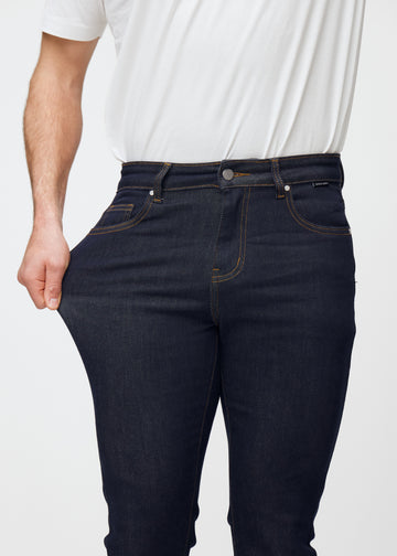 Das Model dehnt die tief dunkelblaue Denim jeans für Herren in der Farbe Midnights am Oberschenkel, um die Dehnbarkeit des Materials zu zeigen.