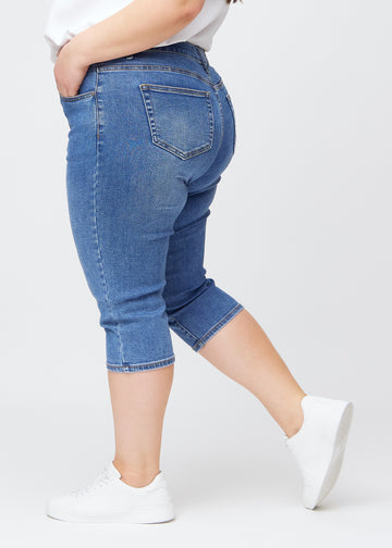 Blå denim slim capris i farven Rivers – set fra siden på en plus-size model, så man ser pasform og silhuet.