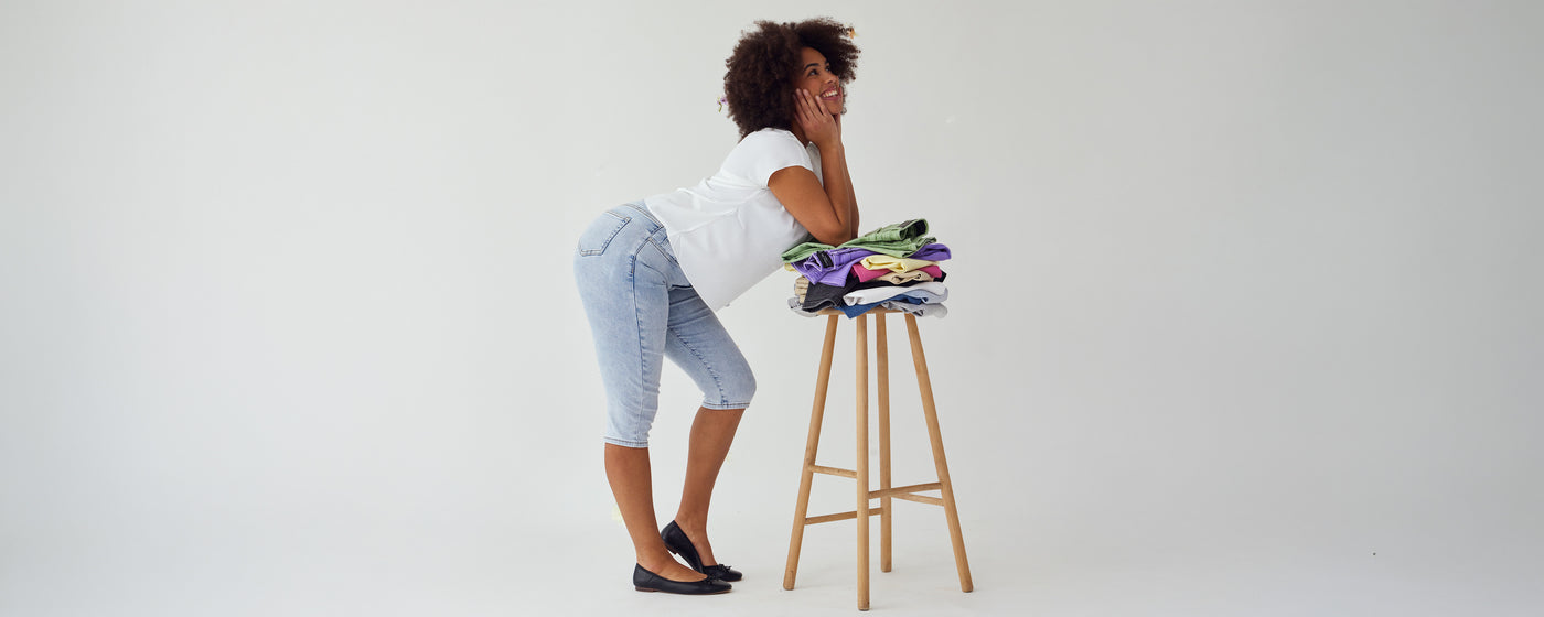 Kvinde iført lyseblå denim capris, med en stak farvede capris på en skammel