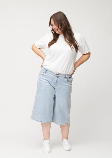 Plus-size model viser løse, lyseblå denim capris i farven Waves i bevægelse og demonstrerer pasform og materiale.