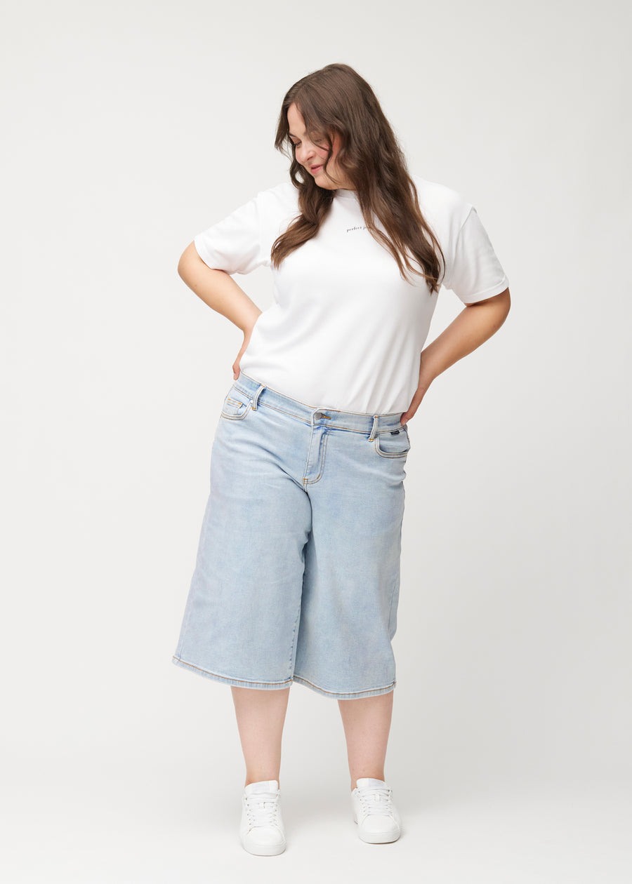 Plus-size model viser løse, lyseblå denim capris i farven Waves i bevægelse og demonstrerer pasform og materiale.