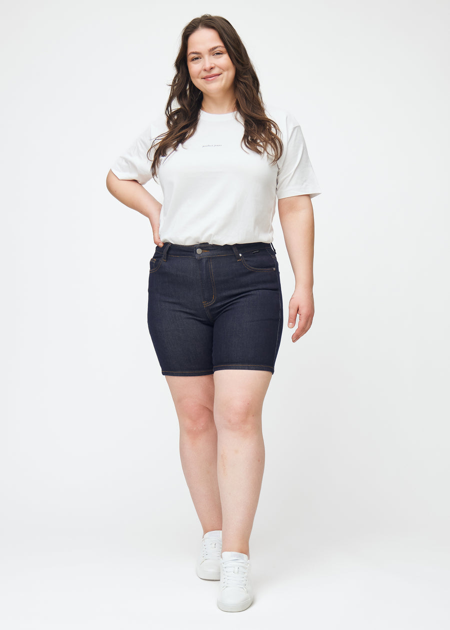 Plus-size model viser dyb mørkeblå denim shorts til kvinder i farven Midnights med skinny pasform i bevægelse.