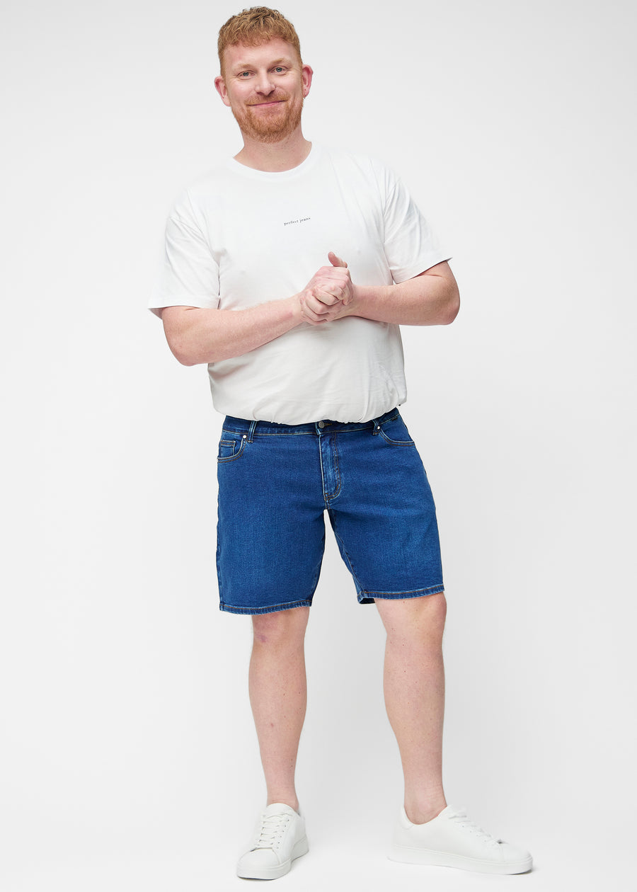 Plus-size model viser mørkeblå denim shorts til mænd i farven Oceans med regular pasform i bevægelse.